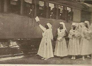 Black soldiers on troop train passing through New Orleans being served chocolates and cigarettes by the Colored Auxiliary of the American  Red Cross (Scott, 1919)